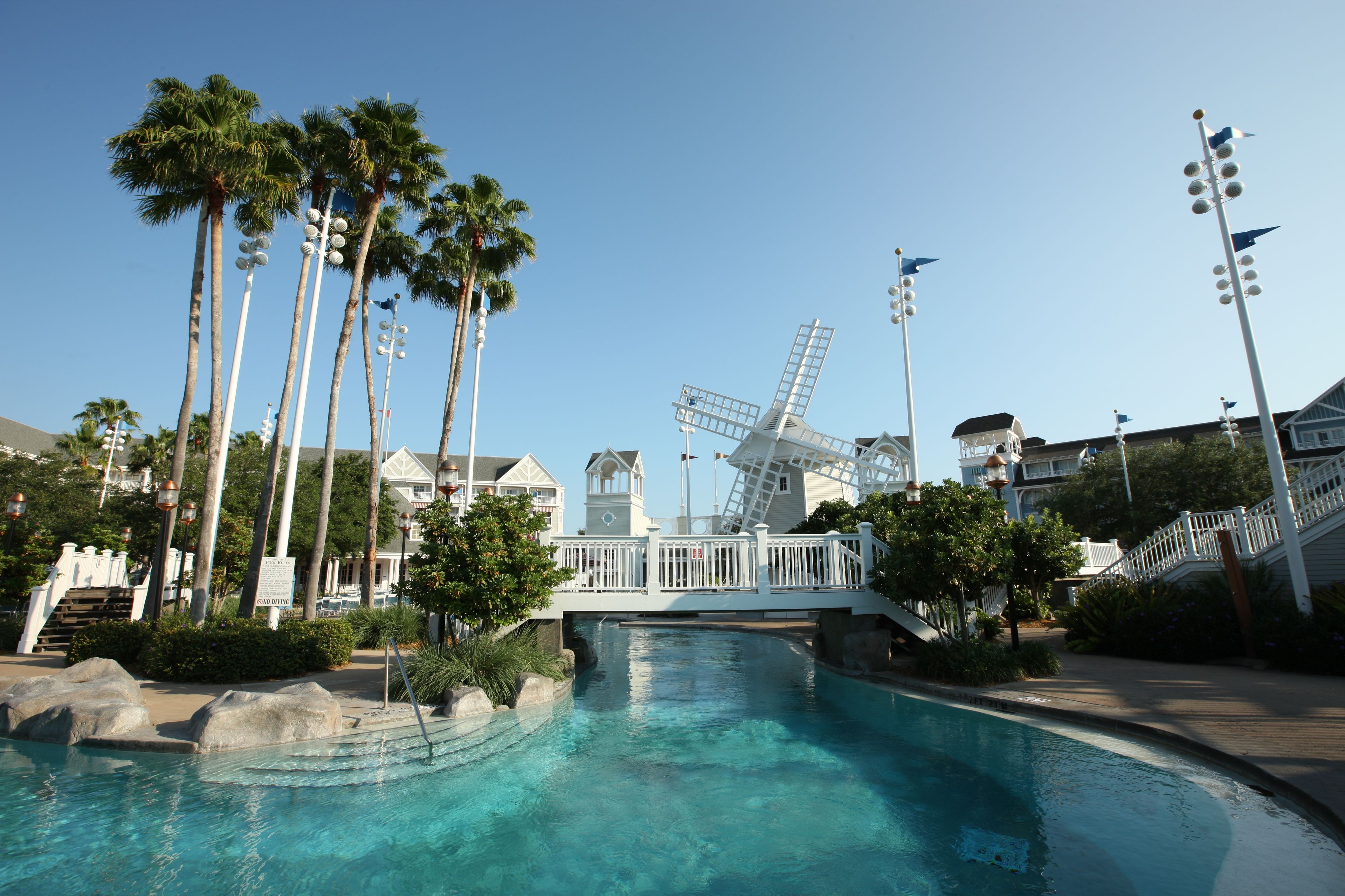 A resort pool area with palm trees, a windmill, and a bridge.