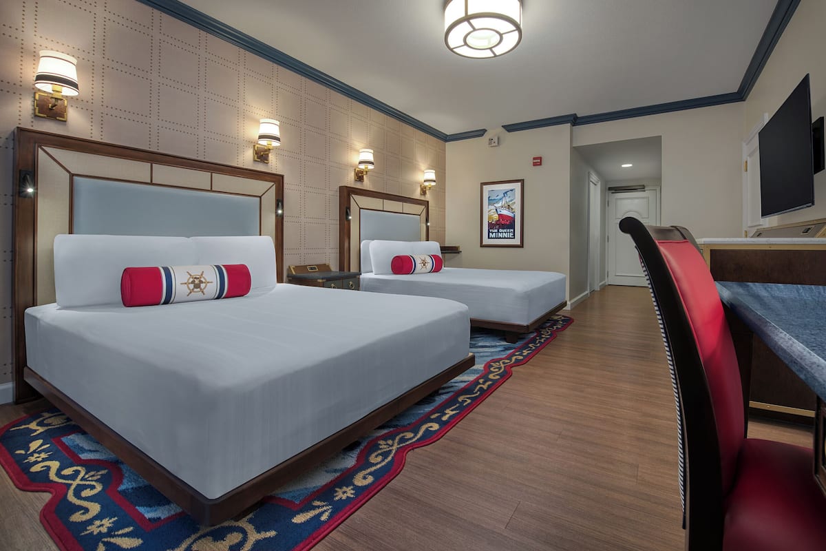 Habitación de hotel con dos camas, un escritorio, una silla y un televisor.