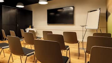 Un salón de conferencias con una pantalla grande, una pizarra y varias sillas dispuestas para una reunión.