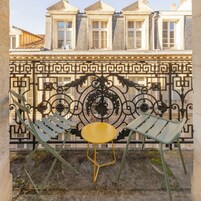 A courtyard with two green metal chairs and a yellow table, surrounded by ornate black metal fencing.
