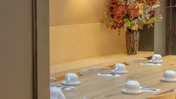 A dining area with a long wooden table set for a meal, a vase of flowers, and a wall-mounted lamp.