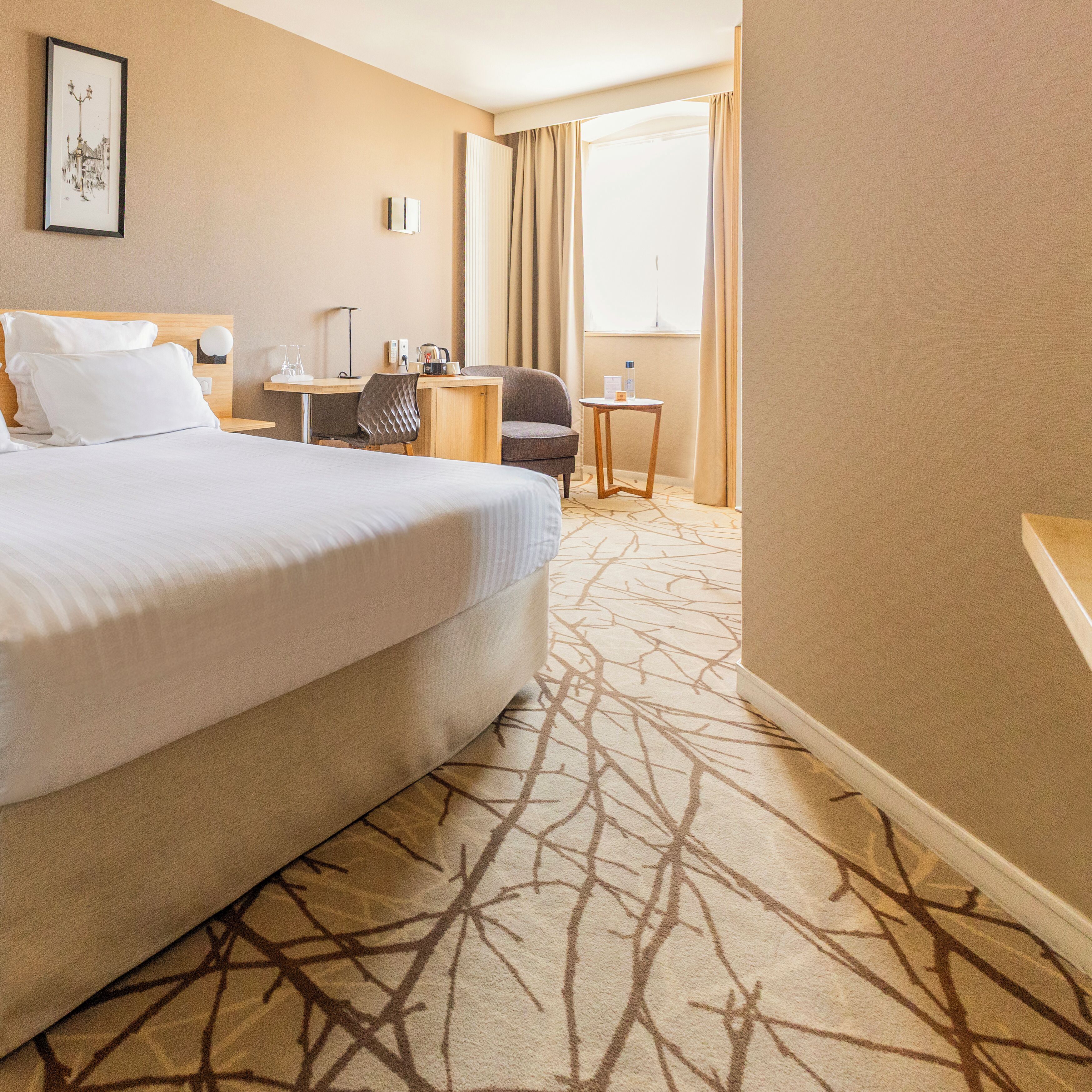 Een hotelkamer met een groot bed, een bureau, een stoel, een klein tafeltje en een schilderij aan de muur.