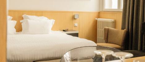 A hotel room with a bed, bedside table, lamp, and a window with curtains.