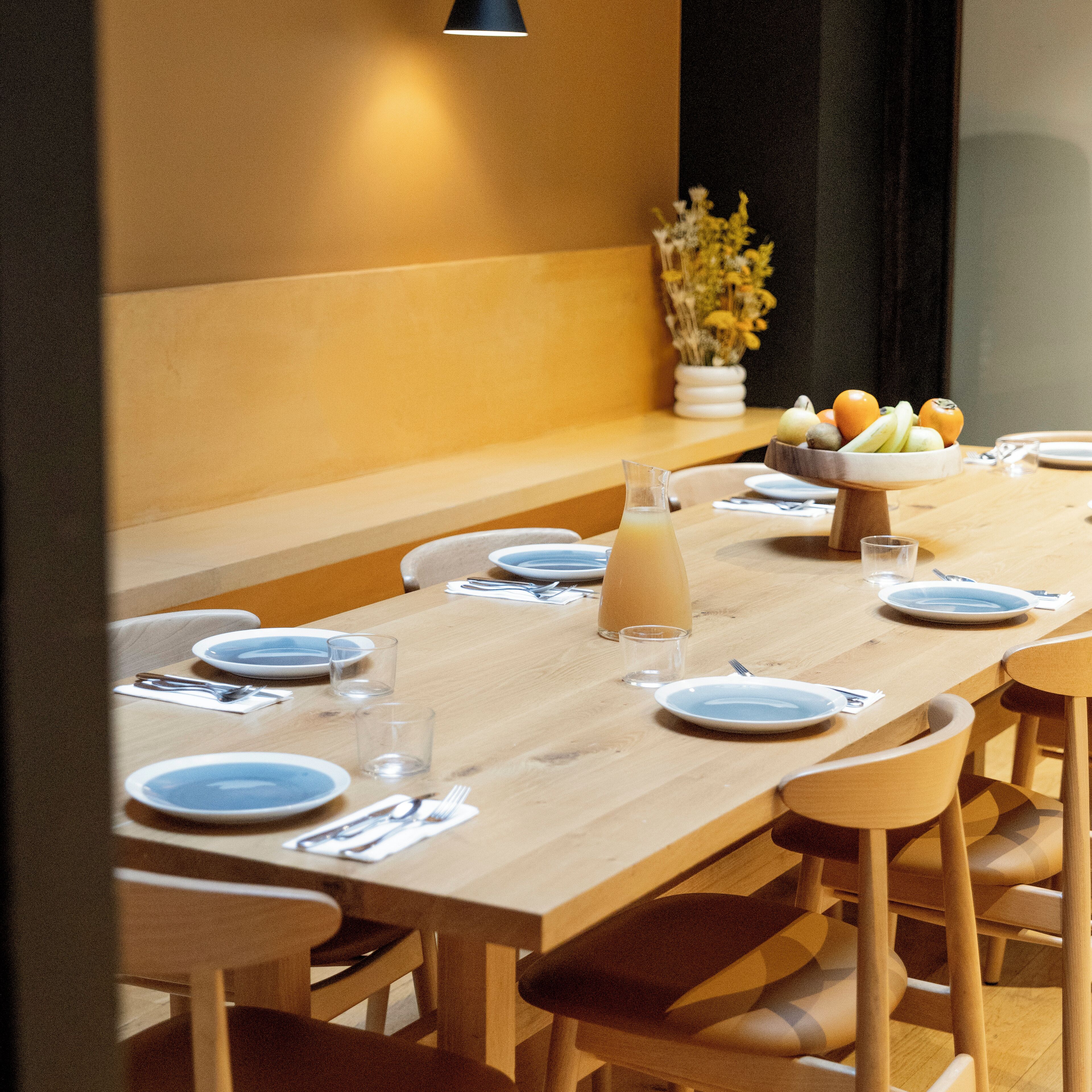Un espace repas avec une longue table en bois dressée pour le repas, entourée de chaises.