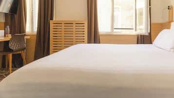 Habitación de hotel con una cama grande, un escritorio con silla, televisión y ventana con cortinas.