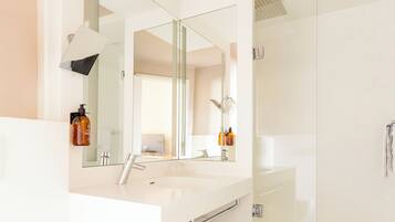 A modern bathroom with a large mirror, a sink, and a glass-enclosed shower.