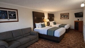 A hotel room with two beds, a sofa, a television, and framed posters on the wall. - Sturgis Lodge & Suites, Travelodge by Wyndham (Sturgis)