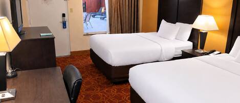 A hotel room with two beds, a desk, a chair, and a view of an outdoor area.