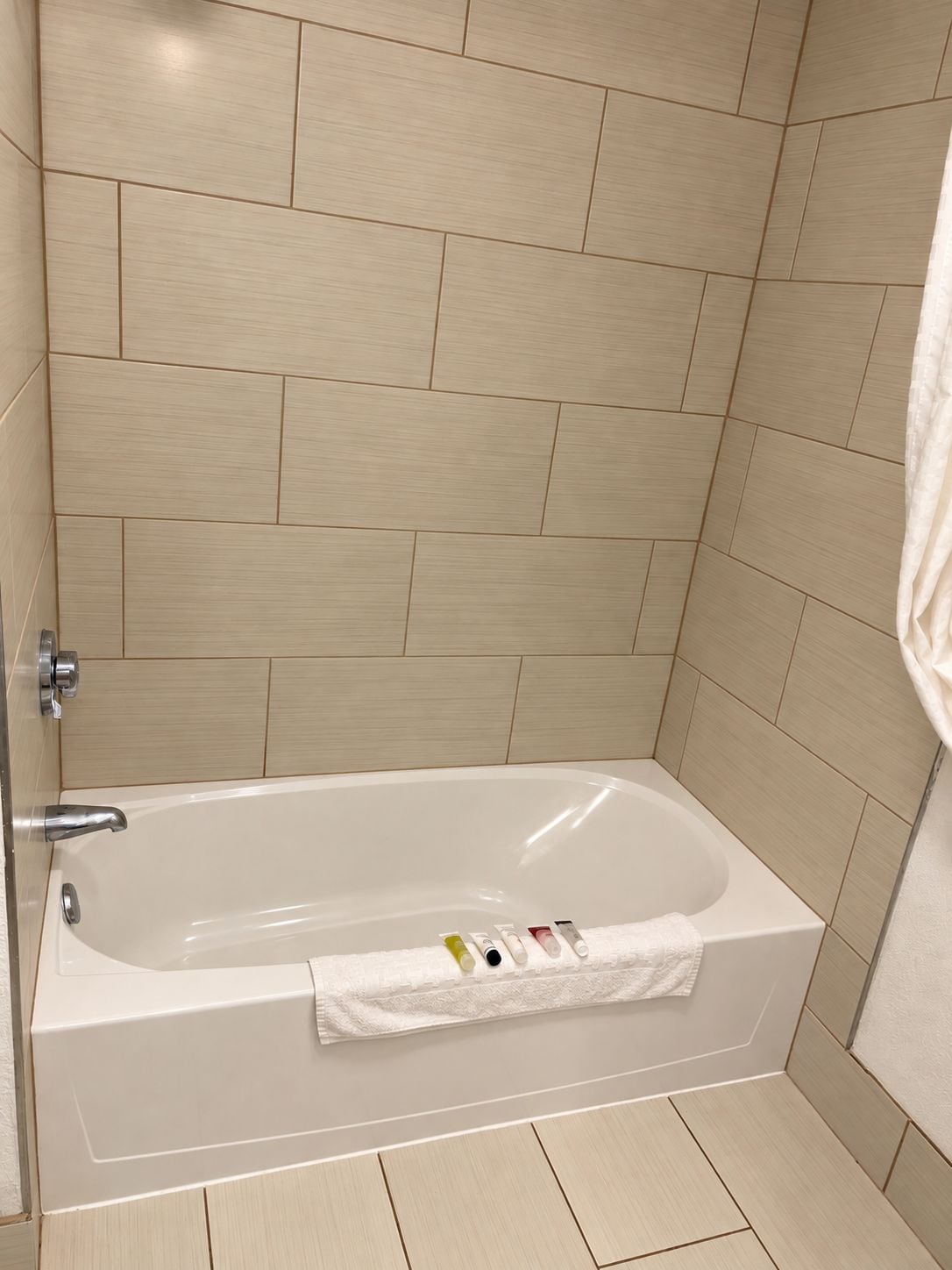A bathroom with a bathtub, tiled walls, and a towel rack with toiletries.