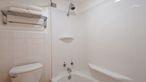 A bathroom with a toilet, a bathtub, and a shower. There is a towel rack with towels on it. - Sturgis Lodge & Suites, Travelodge by Wyndham (Sturgis)