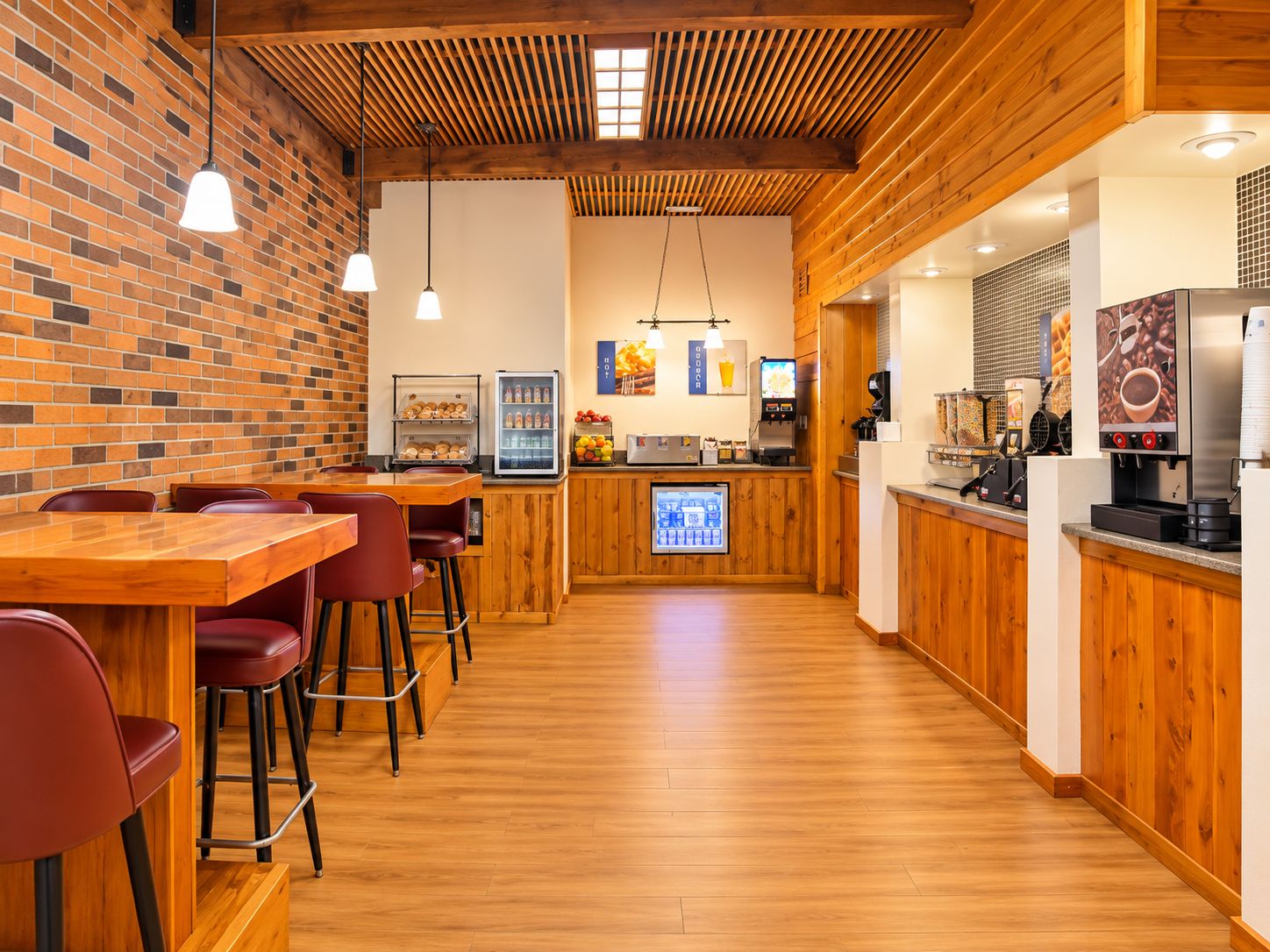 A restaurant interior with wooden flooring, brick walls, and a bar area with stools and a coffee machine.