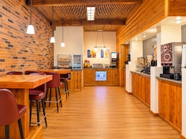 Un interior de restaurante con suelo de madera, paredes de ladrillo y una zona de bar con taburetes y una máquina de café.
