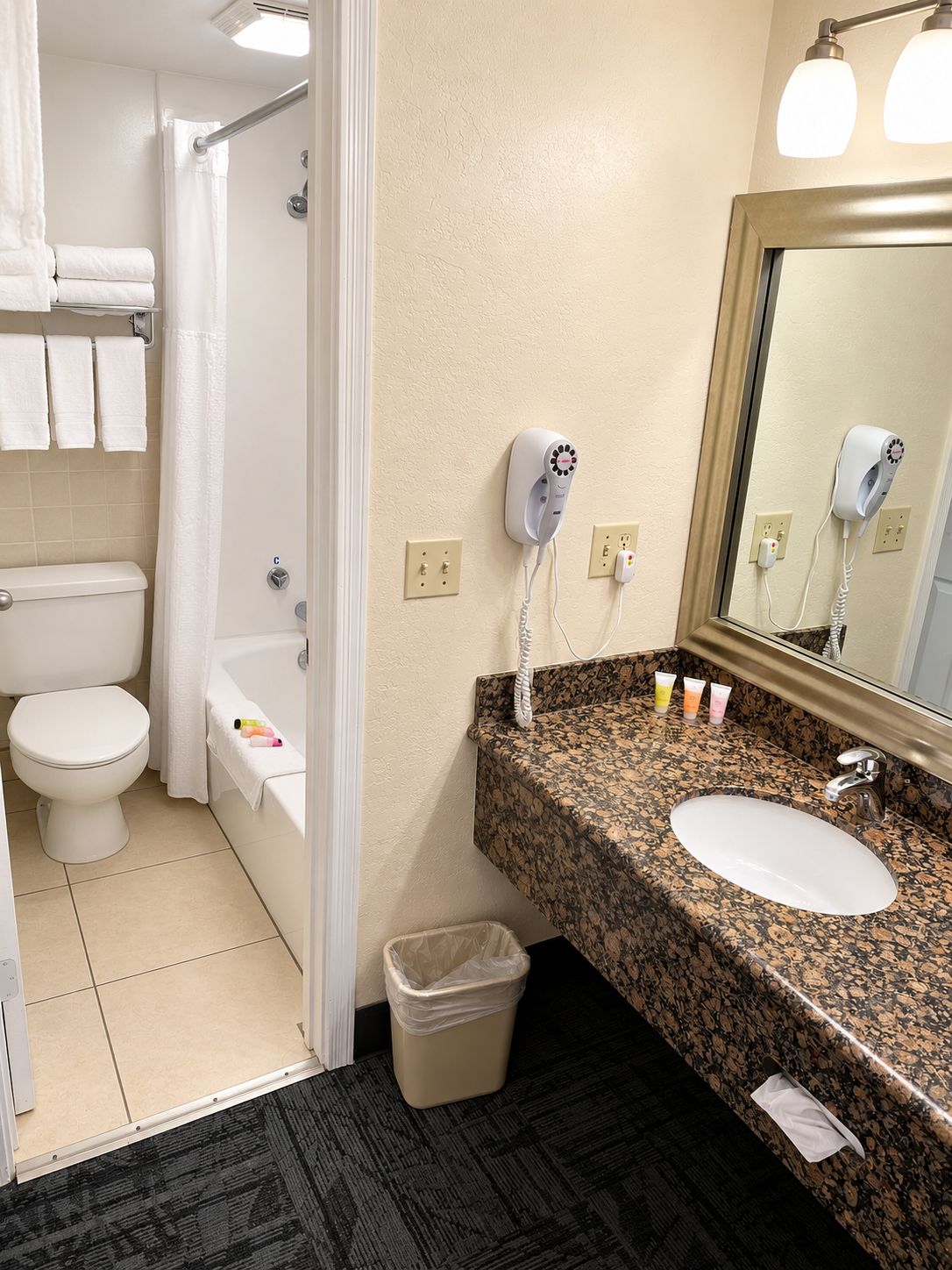 Een badkamer met toilet, bad en wastafel. Er zitten haardroger(s) aan de muur bevestigd.