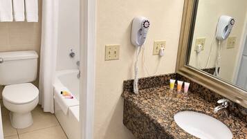 Een badkamer met toilet, bad en wastafel. Er zitten haardroger(s) aan de muur bevestigd.