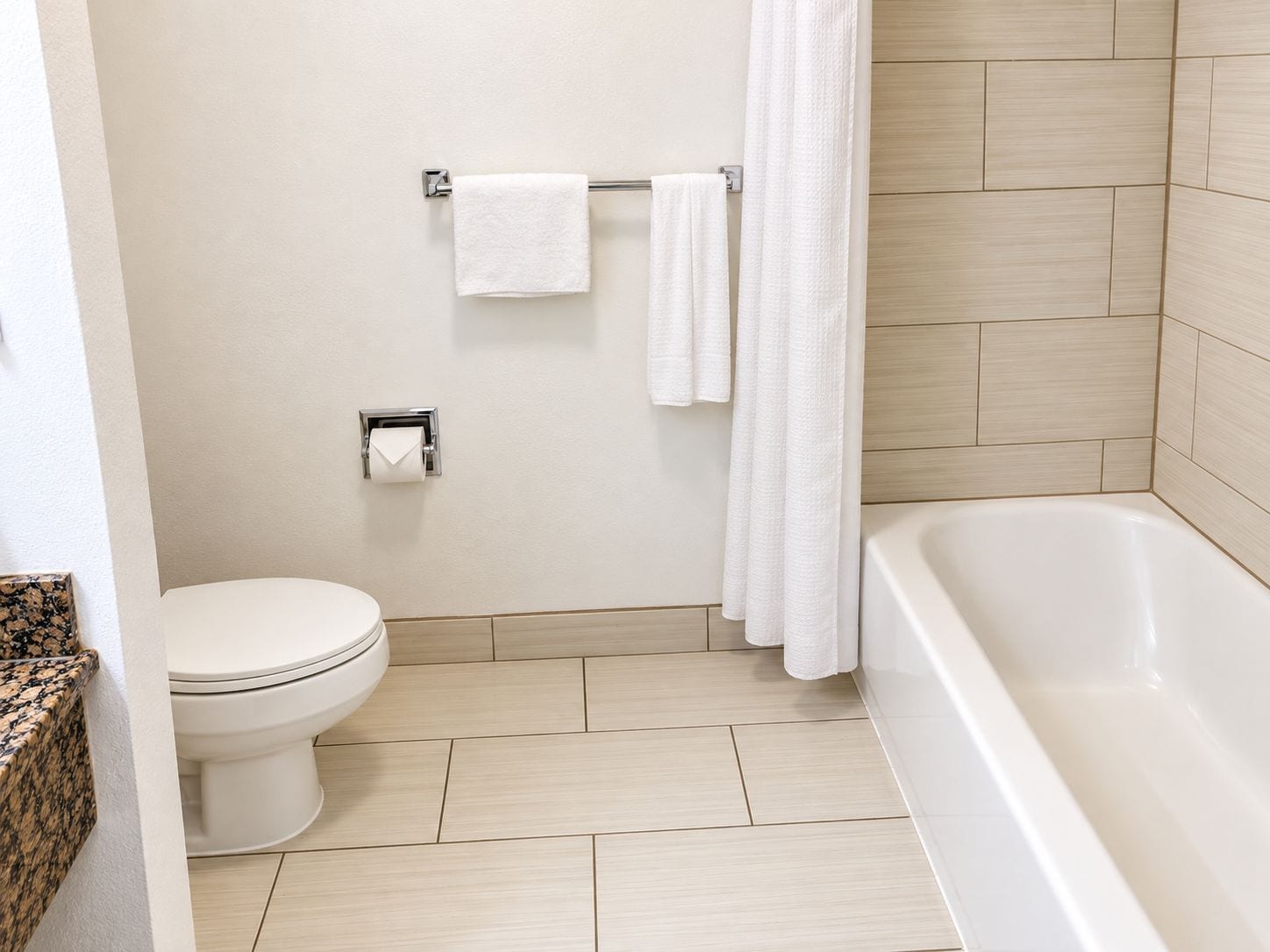A bathroom with a toilet, a towel rack with towels, a toilet paper holder, and a bathtub.