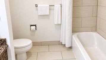 A bathroom with a toilet, a towel rack with towels, a toilet paper holder, and a bathtub.
