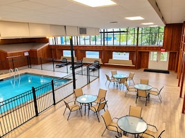 Una piscina interior con cubierta de madera, rodeada de mesas y sillas, y amplias ventanas que ofrecen vistas al exterior.