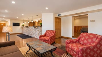 Un vestíbulo de hotel con una recepción, un área de estar con sillones y una mesa de centro, y un televisor montado en la pared.
