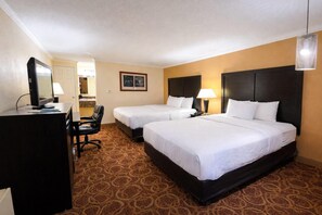 A hotel room with two beds, a desk, a chair, a desk lamp, and a hanging light fixture. - Sturgis Lodge & Suites, Travelodge by Wyndham (Sturgis)