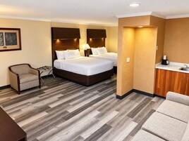 A hotel room with two beds, a chair, a desk, and a kitchenette.
