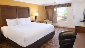 A hotel room with a large bed, a desk, a chair, a lamp, and a window with curtains. - Sturgis Lodge & Suites, Travelodge by Wyndham (Sturgis)