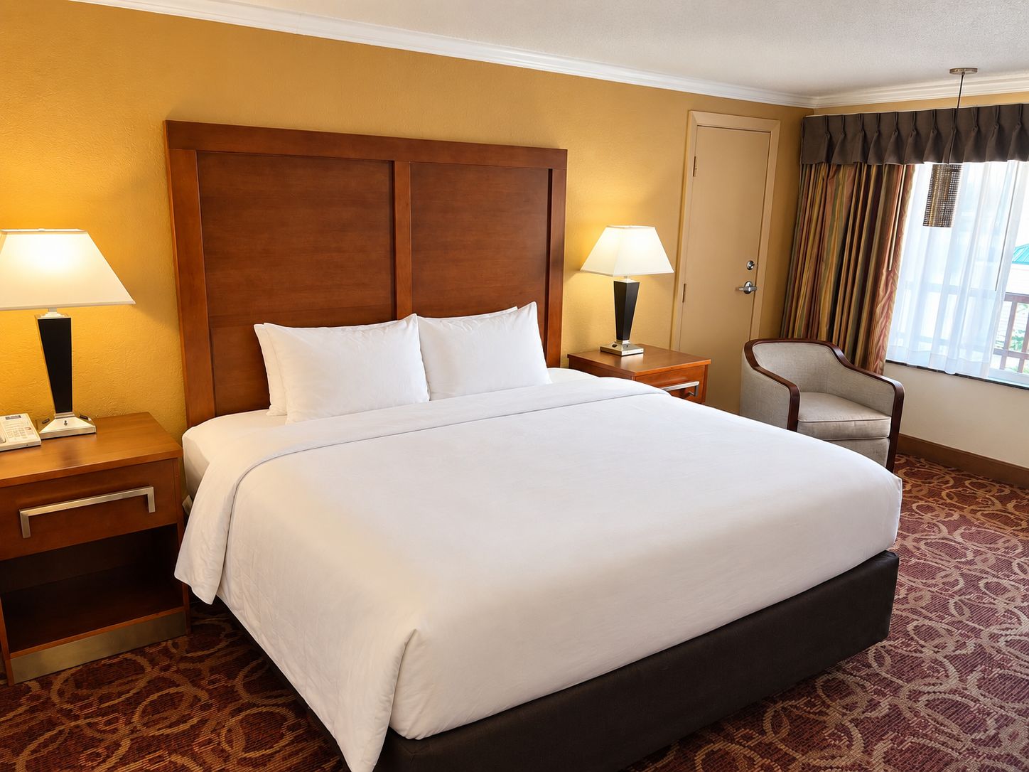 Habitación de hotel con una cama grande, dos mesitas de noche con lámparas, una silla y una puerta.