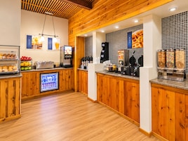 Una barra de desayuno con mostrador refrigerado, tostadora, máquina para gofres y dispensadores de bebidas.