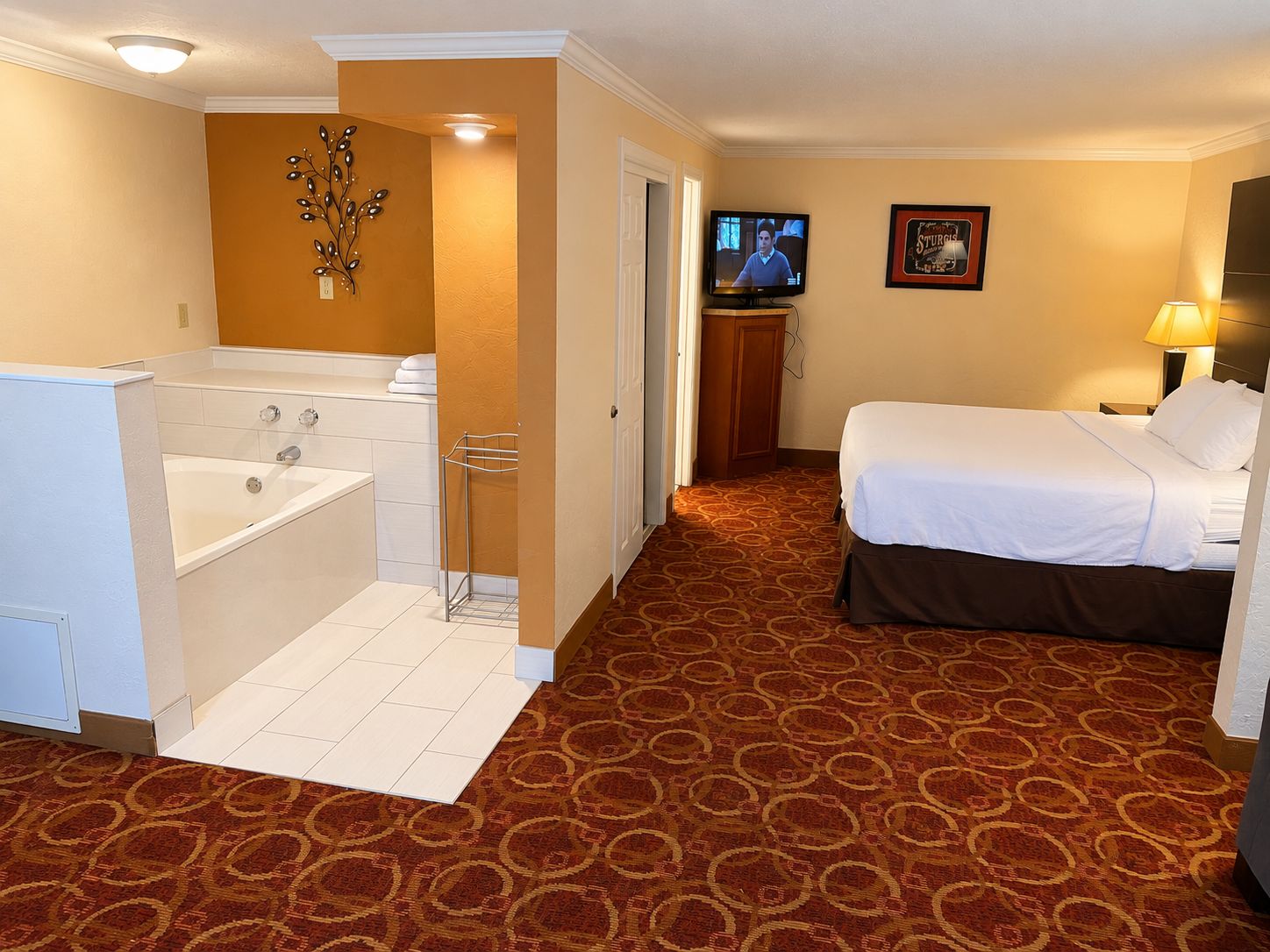 A hotel room with a bathtub, a bed, a television, and a carpeted floor.