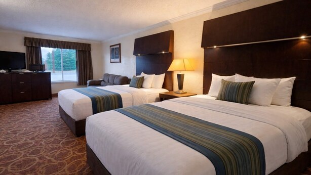 A hotel room with two beds, a TV, a desk, and a window with curtains. - Sturgis Lodge & Suites, Travelodge by Wyndham (Sturgis)