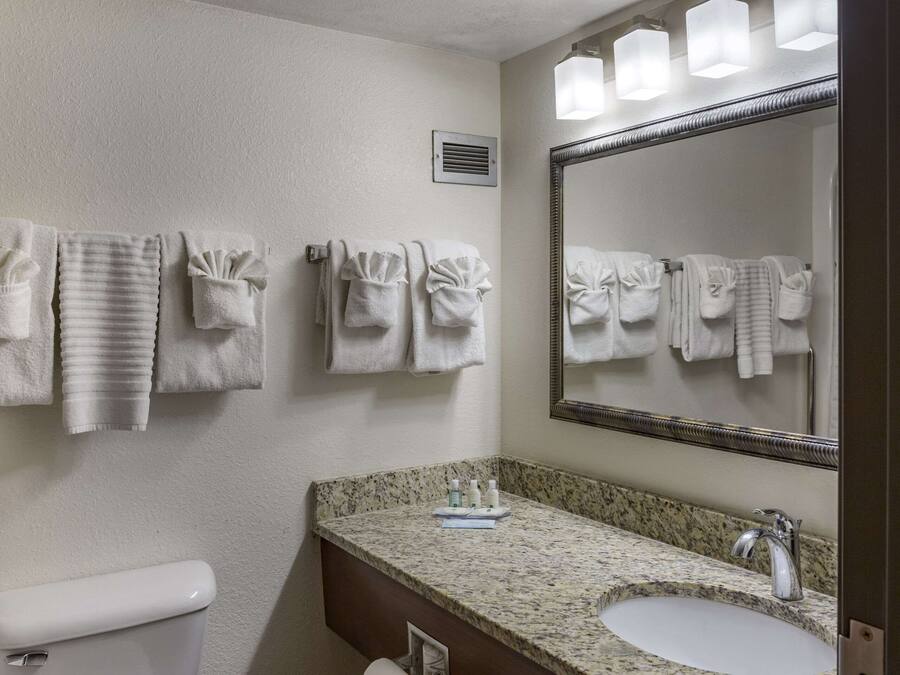 Un baño con inodoro, lavamanos y espejo. Hay toallas colgadas en la pared y un extractor sobre el inodoro.