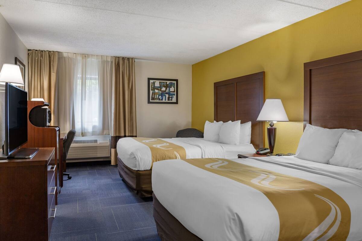 A hotel room with two beds, a desk, a TV, and a painting on the wall.