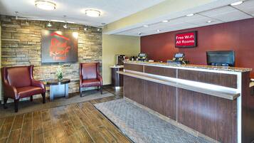 Zona de recepción de Red Roof Inn con pared de piedra, sillas de cuero, un mostrador de recepción y un cartel que indica Wi-Fi gratuito en todas las habitaciones.