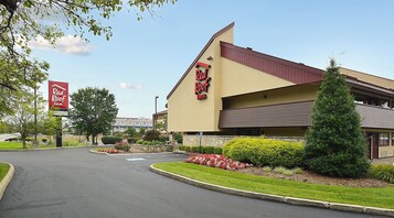 Un hotel Red Roof Inn con un letrero grande, estacionamiento y áreas ajardinadas con arbustos y un pequeño árbol.