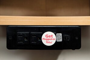 A black electrical outlet with a white plug-in card that reads 'Get Plugged-In! RedRoof.' - Red Roof Inn Louisville East - Hurstbourne (Louisville)