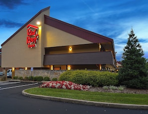 A Red Roof Inn with a flat roof, a parking lot, and a landscaped garden with red and white flowers. - Red Roof Inn Louisville East - Hurstbourne (Louisville)