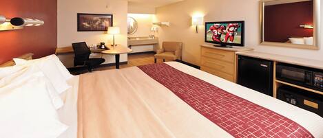 A hotel room with a large bed, a desk with a chair, a television, and a minibar.