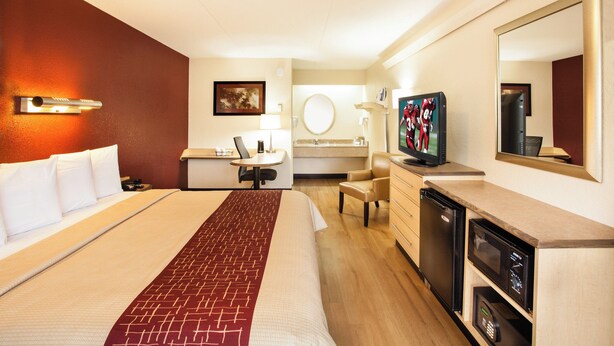 A hotel room with a bed, desk, chair, television, and a mirror. - Red Roof Inn Louisville East - Hurstbourne (Louisville)