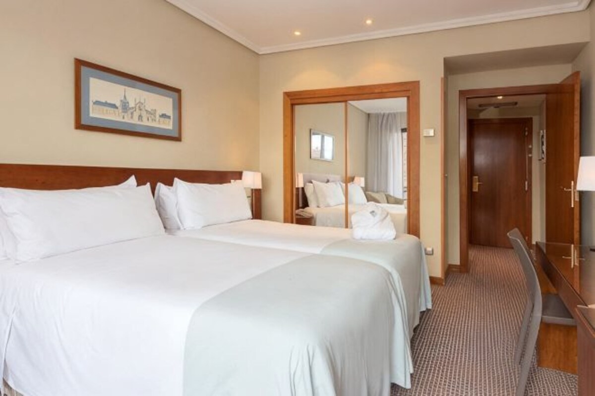 Een hotelkamer met twee bedden, een grote spiegel, een houten hoofdeinde en een vloerbedekking.