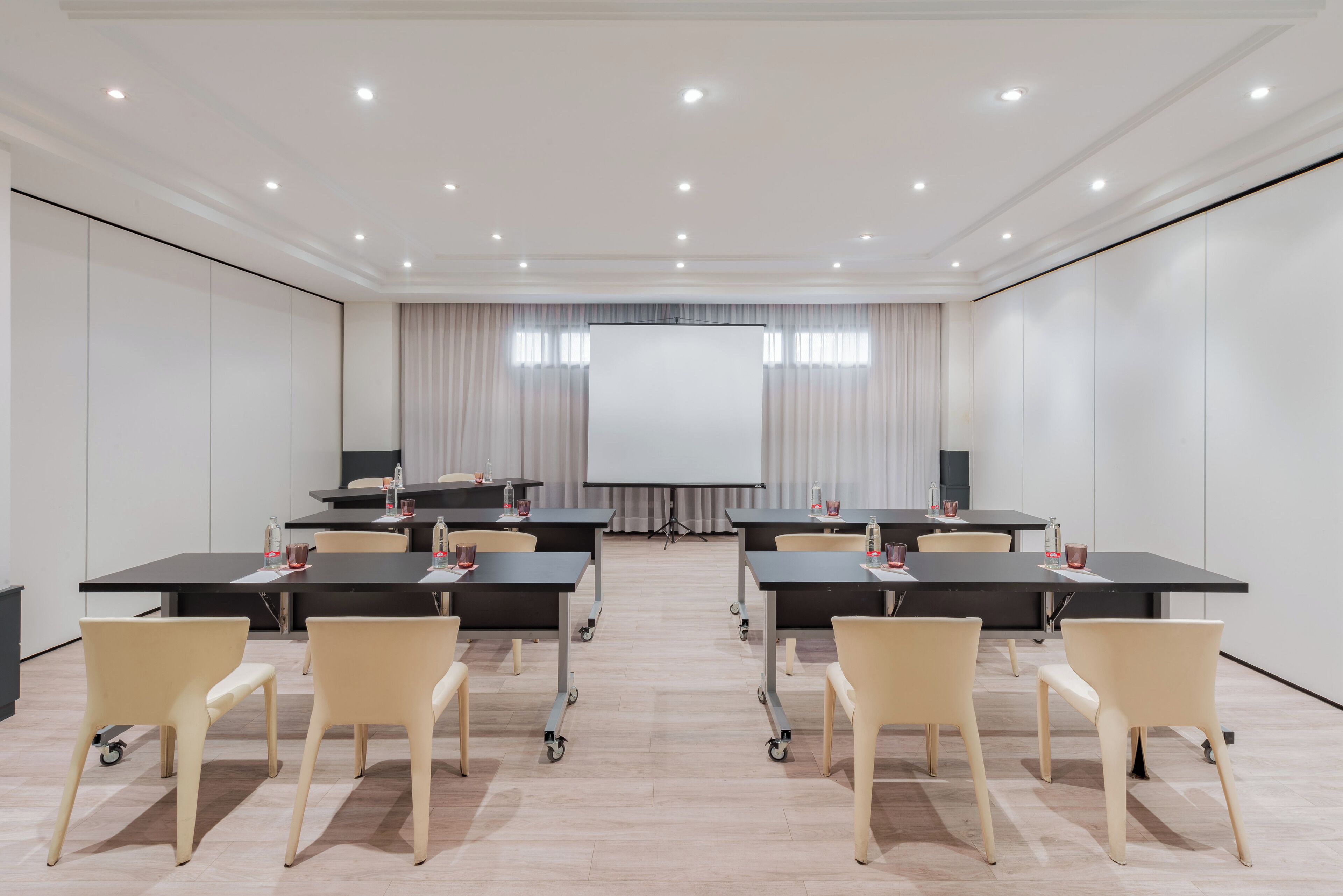 A conference room with a large screen, tables, chairs, and a projector.