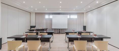 A conference room with a large screen, tables, chairs, and a projector.