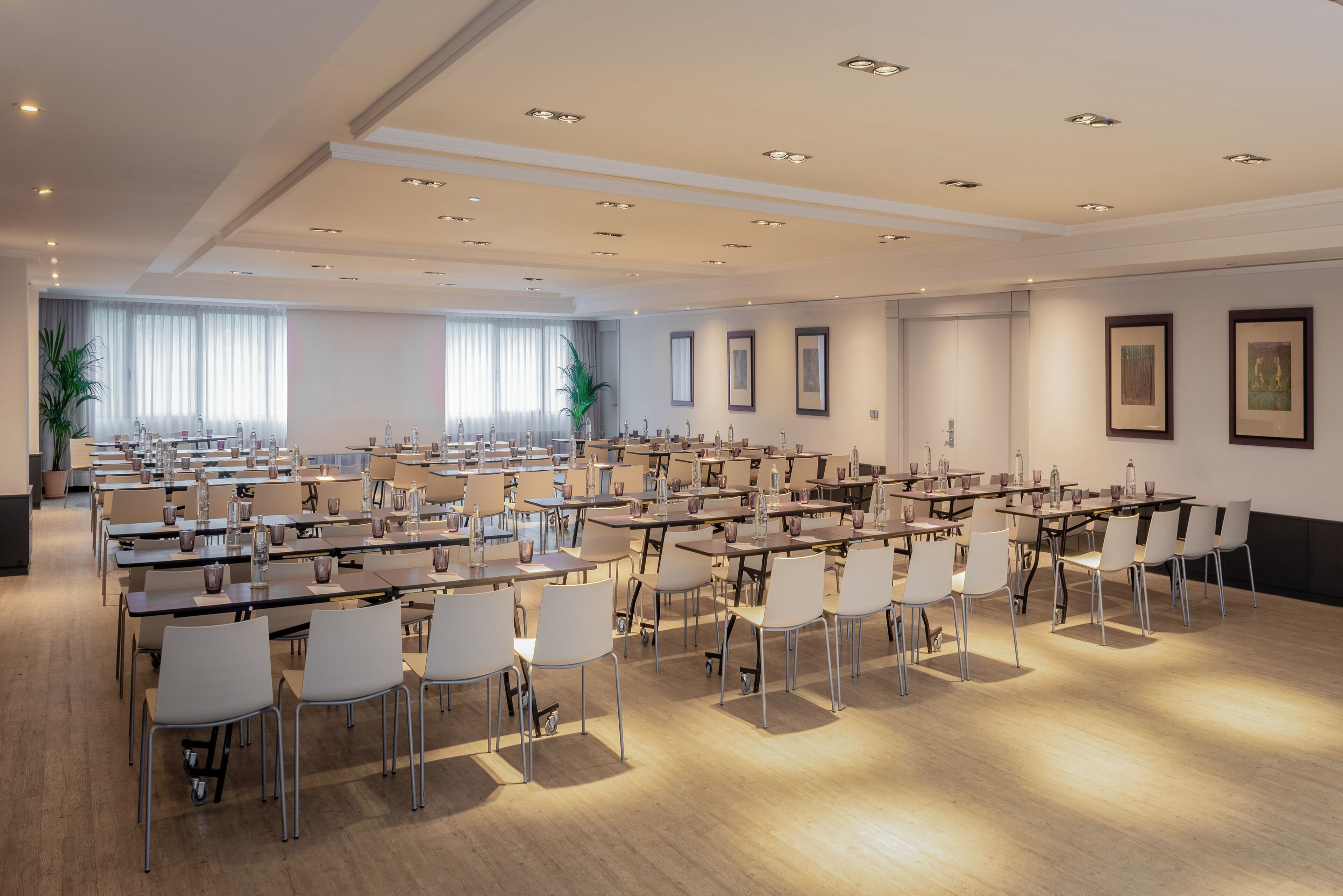 A large conference room with multiple tables and chairs, equipped with water dispensers and glassware.
