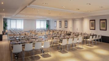 A large conference room with multiple tables and chairs, equipped with water dispensers and glassware.