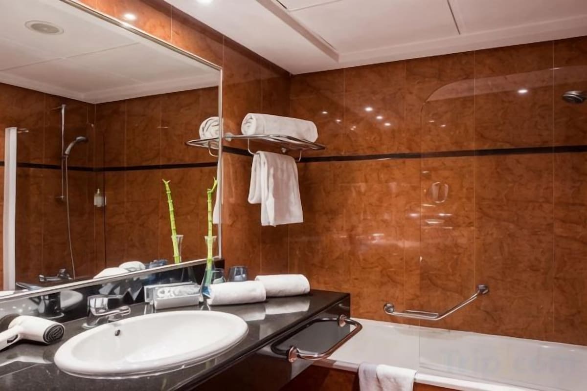 A modern bathroom with a large mirror, a sink, a shower, and a towel rack.