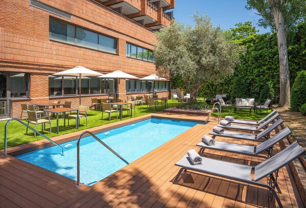 Zwembad met ligbedden en parasols, omgeven door een gebouw van baksteen met terras en een verzorgd gazon.