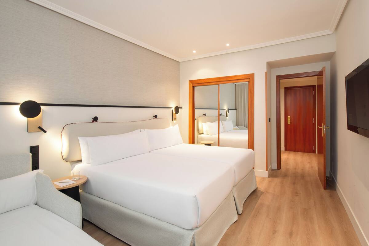 Hotellihuone, jossa on suuri sänky, yöpöydät, peili ja televisio.