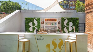 Un espace bar avec un comptoir blanc, deux tabourets de bar en bois et un mur vert orné d’un logo.