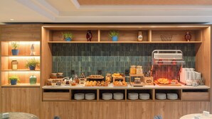 Un comptoir pour le petit-déjeuner propose une variété d’aliments et une machine à café. Des étagères accueillent des plantes et des objets décoratifs.