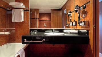 A modern bathroom with a black vanity, a large mirror, a white sink, a bathtub, and a towel rack.
