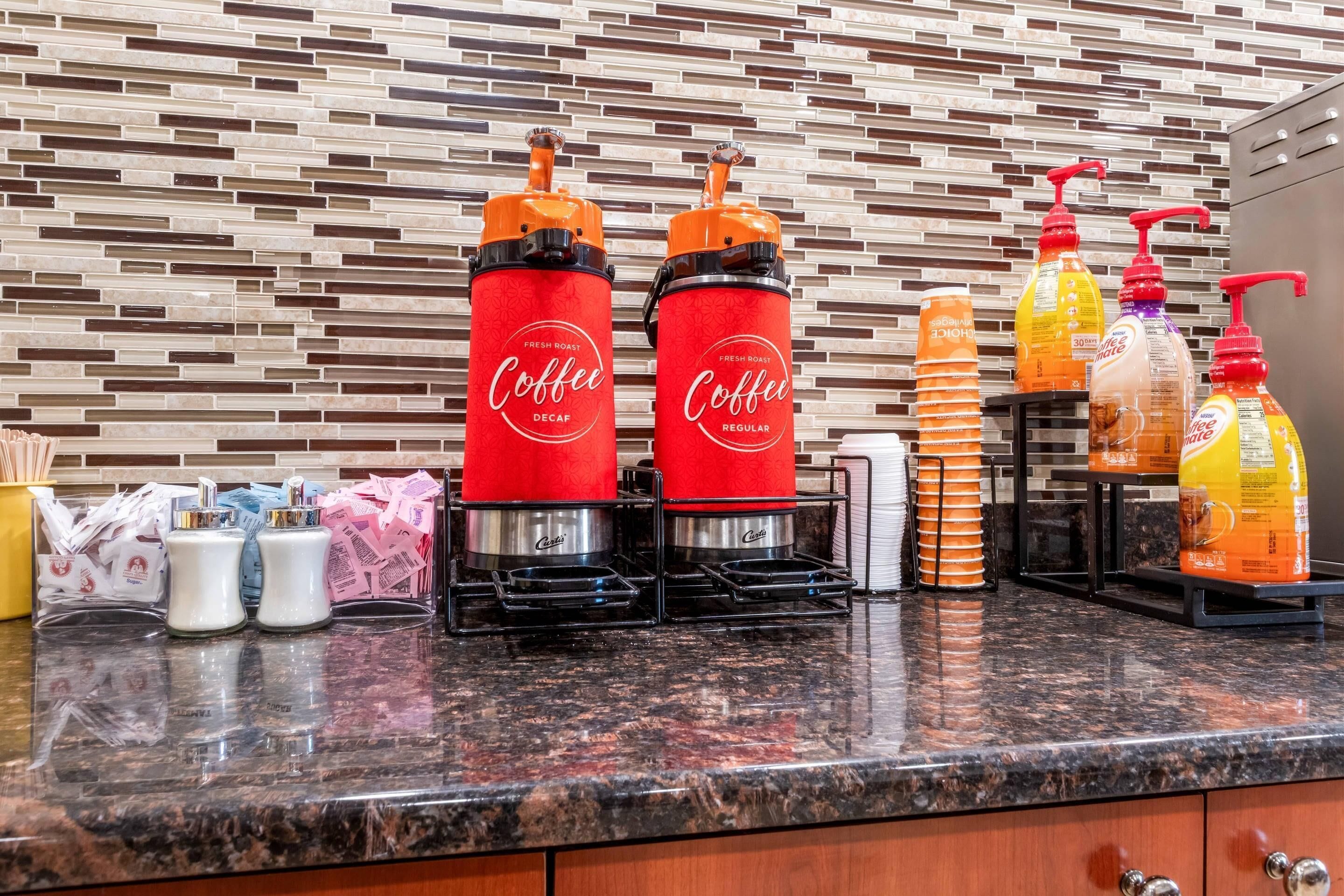 A coffee station with two coffee dispensers, a coffee grinder, and various coffee pods and accessories on a granite countertop.