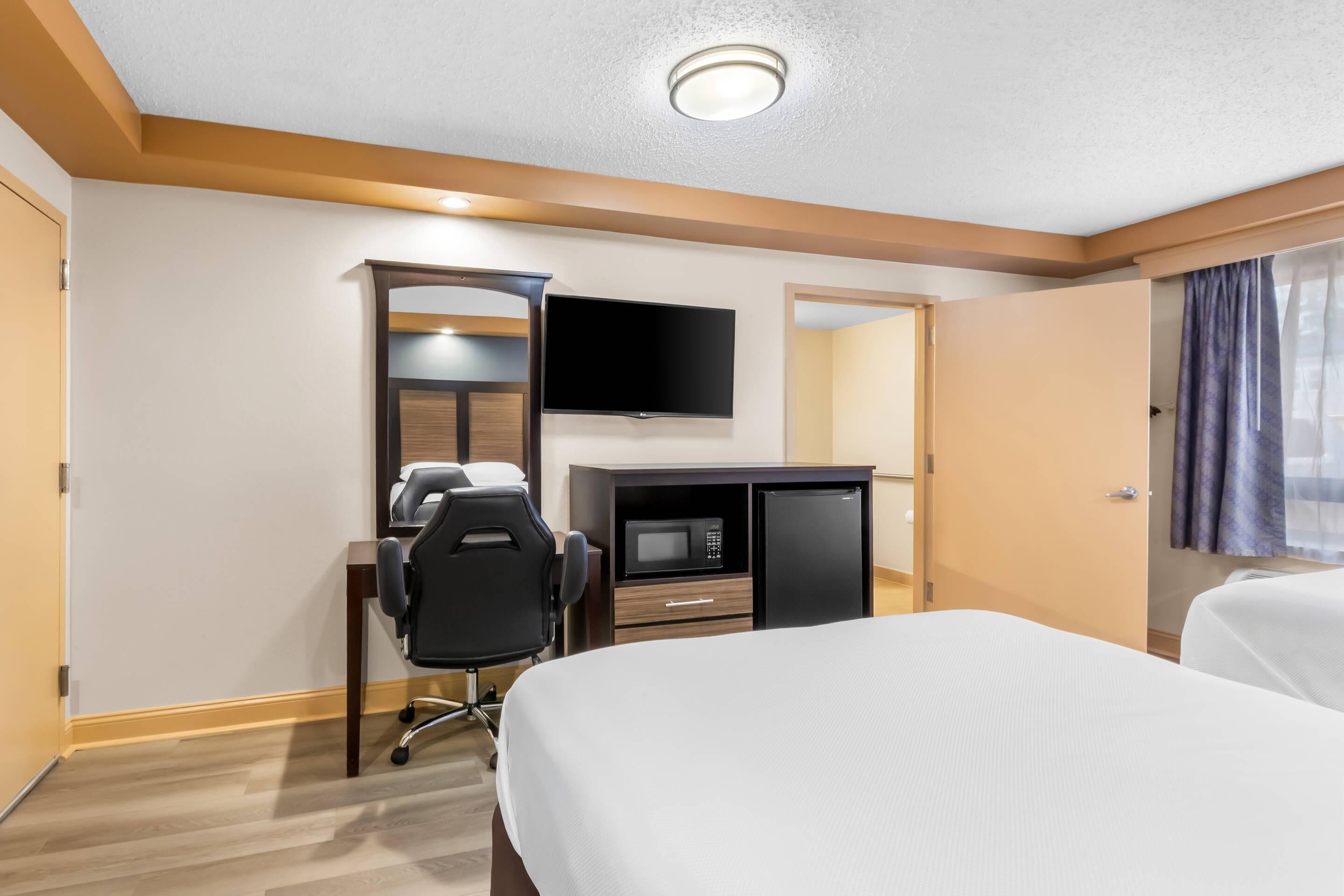 Quarto de hotel com cama, escrivaninha, cadeira, televisão e micro-ondas.